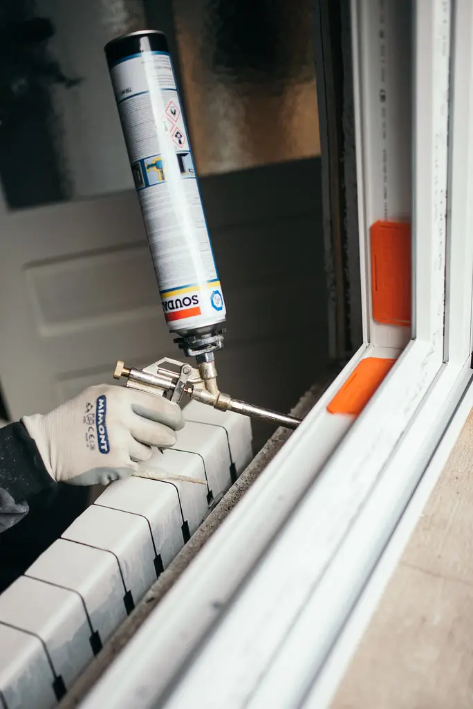 Fitter sealing the gap around a new white window frame with expanding foam