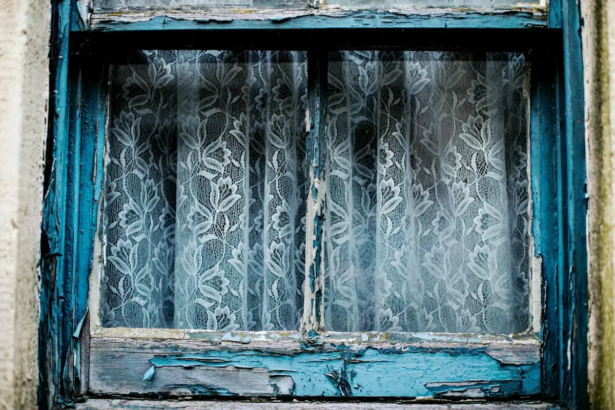 Old timber window with peeling blue paint and lace curtains