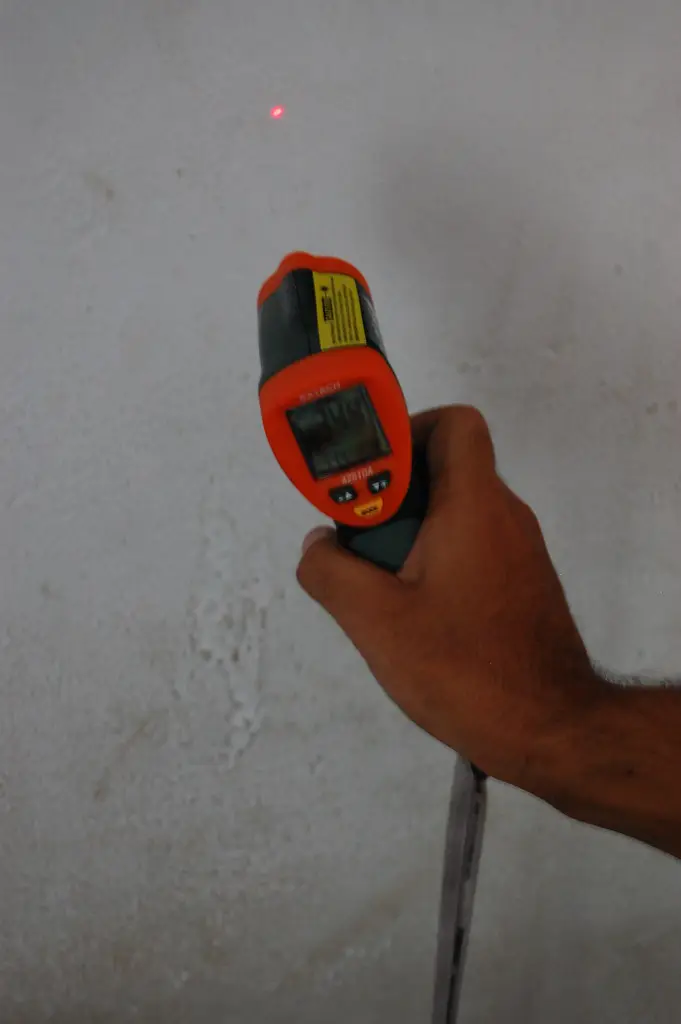 Hand aiming an infrared thermometer at a wall, with the laser dot visible