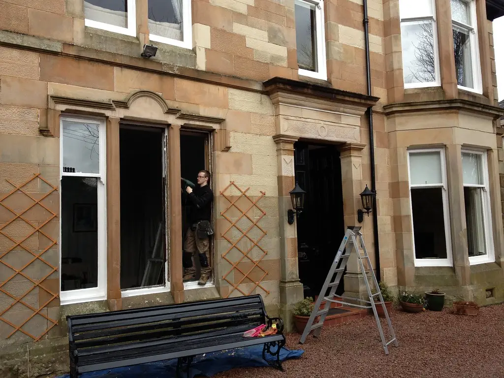 Window fitter standing in a newly opened window frame on a stone house, seen from outside